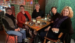 Five women sit around a dinner table looking at the camera.