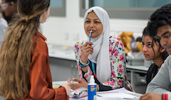 Students sit at a table in the classroom engaging in discussion.